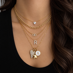 Layered gold necklaces with diamond initial, evil eye, heart and star charms worn on model